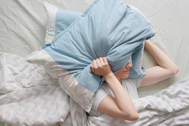 女性はベッドに横になり、不眠症や睡眠に苦しむ枕で頭を覆います