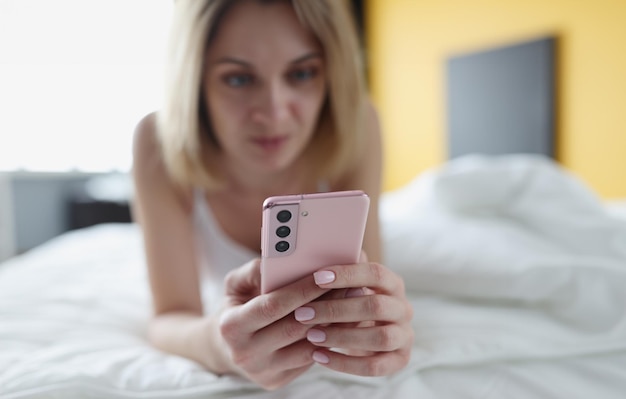 Woman lies in bed and looks at smartphone closeup