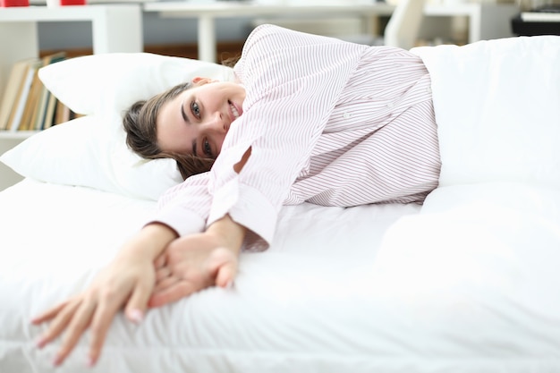 Woman lies in bed in shirt and smiles.