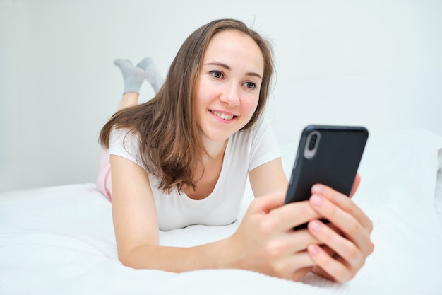 A woman lies on the bed smiling at the phone