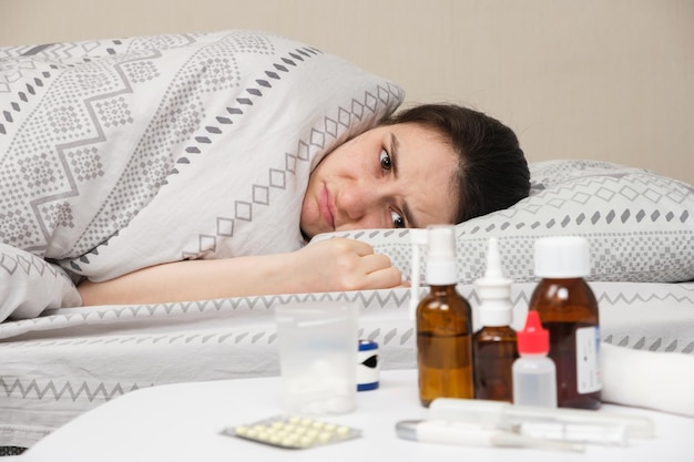 A woman lies in bed and a table with medicines