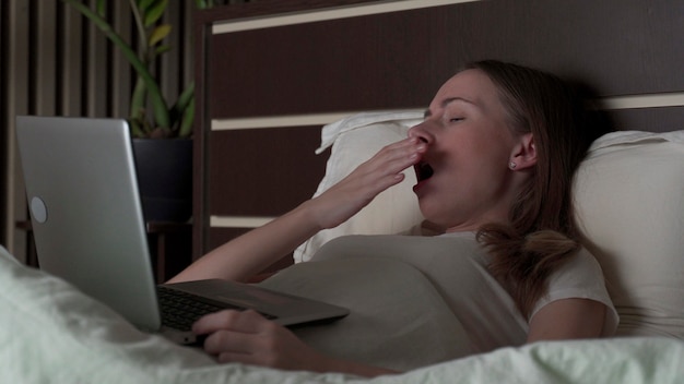 The woman lies on the bed with a laptop and yawns several times, then falls asleep. I try to work at night.