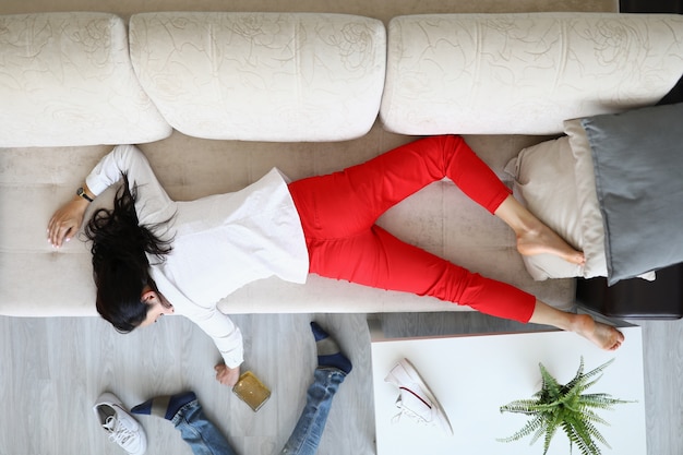 Woman lies on couch and holds bottle of alcohol in her hand