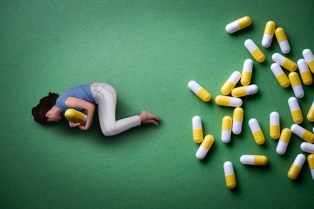 A woman lies on the floor and embraces a capsule of medicine