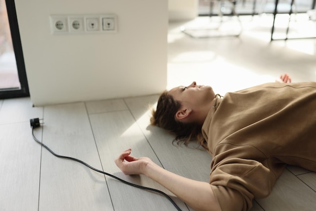 Woman lies on the floor with her eyes closed near electric cable with plug concept of dangerous