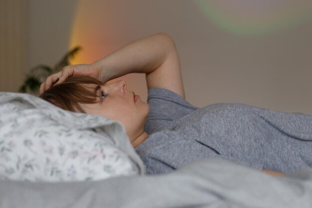 Photo woman lies on her back in bed and has a headache