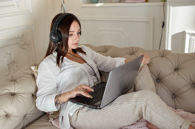 Woman lies at home on the couch with headphones on and listens to music. Day off at home, relax and rest