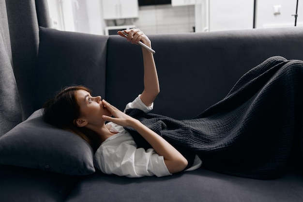 Woman lies on a pillow with a mobile phone in her hand and a gray sofa interior