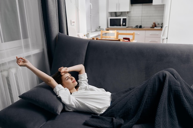 Woman lies on the sofa in the room rest gray plaid kitchen in the background