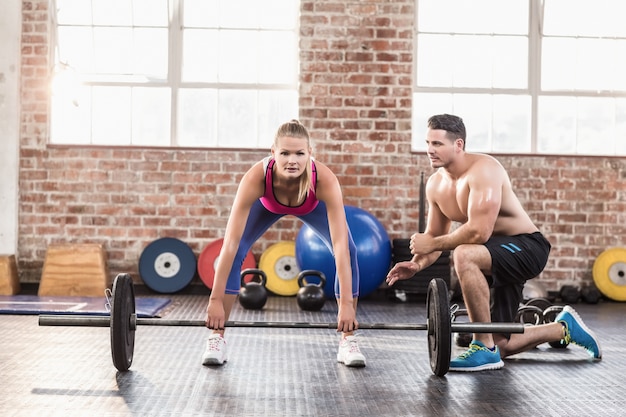 Woman lifting barbell with her trainer at crossfit session