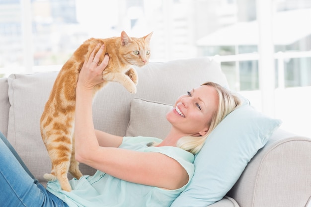 Женщина, поднимающая кошку на диване у себя дома