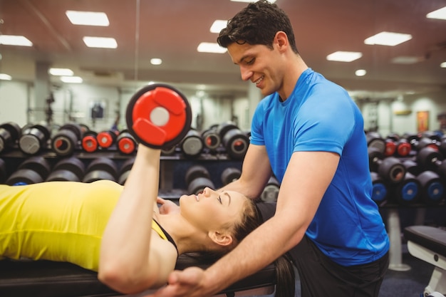 Donna che alza dumbbells con il suo allenatore