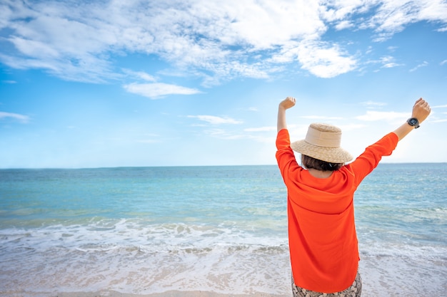 女性の手を持ち上げて、青い海を背景に熱帯の海の景色を探しています。