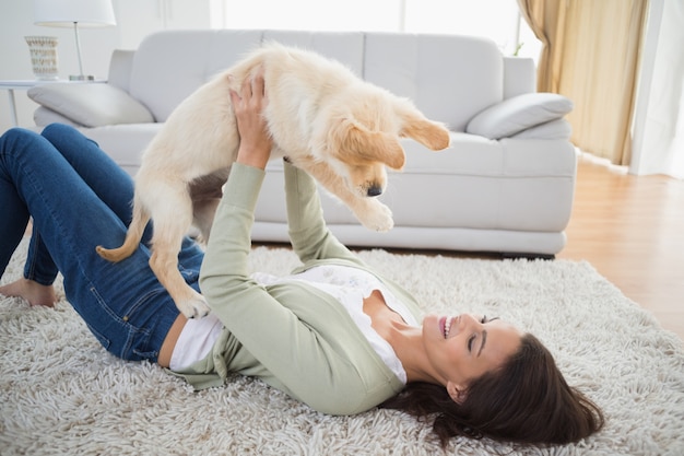 Woman lifting puppy while lying on rug