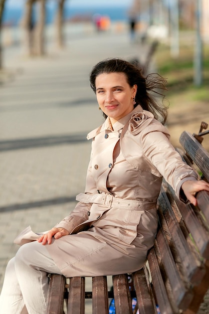 a woman in a light raincoat is sitting on a bench