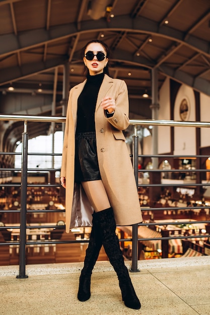 Женщина в легком шерстяном пальто и длинных сапогах