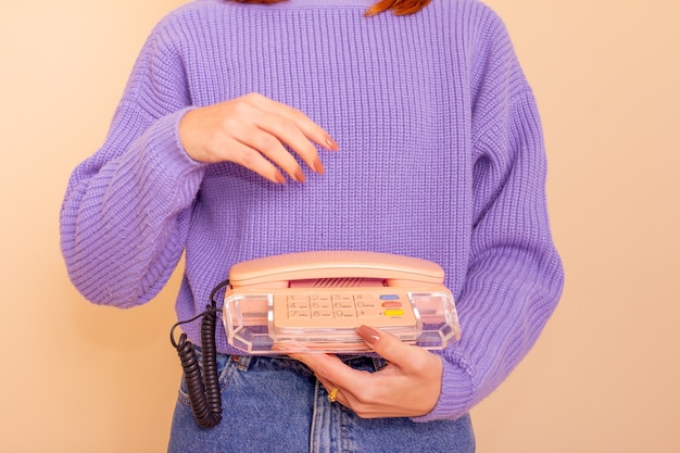 Woman in lilac sweater, jeans and socks holding a phone. Beige background.