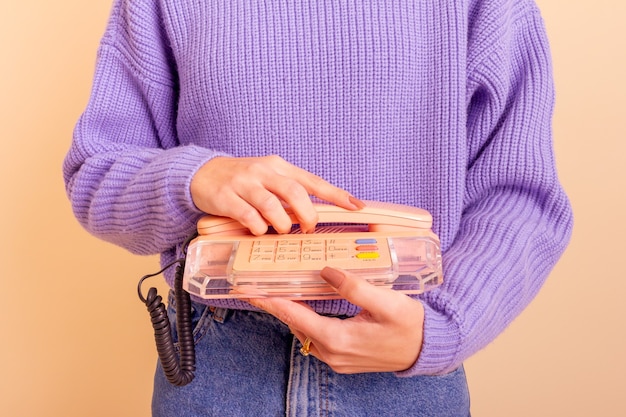 Woman in lilac sweater, jeans and socks holding a phone. Beige background.