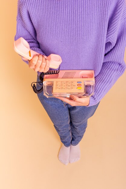 Woman in lilac sweater, jeans and socks holding a phone. Beige background.