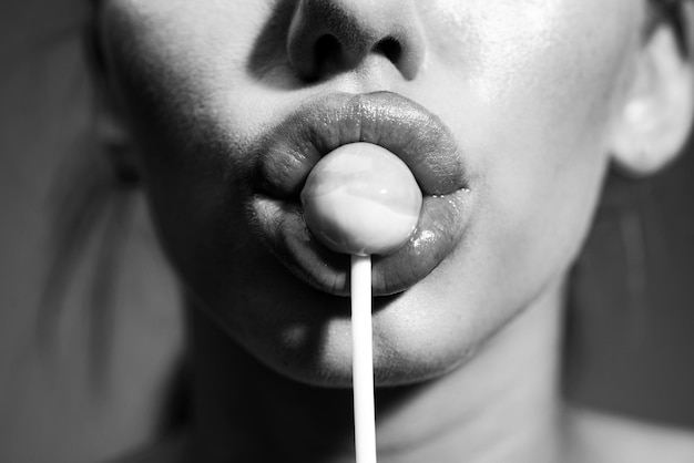 Woman lips sucking lollypop woman holding lollipop in mouth\
close up red lips sensual and sexy concept