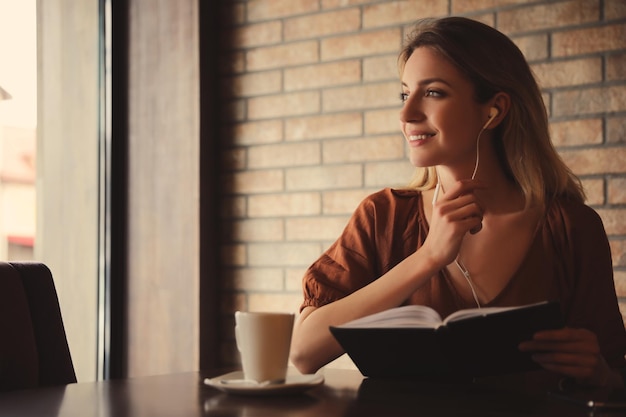 Женщина слушает аудиокнигу за столом в кафе