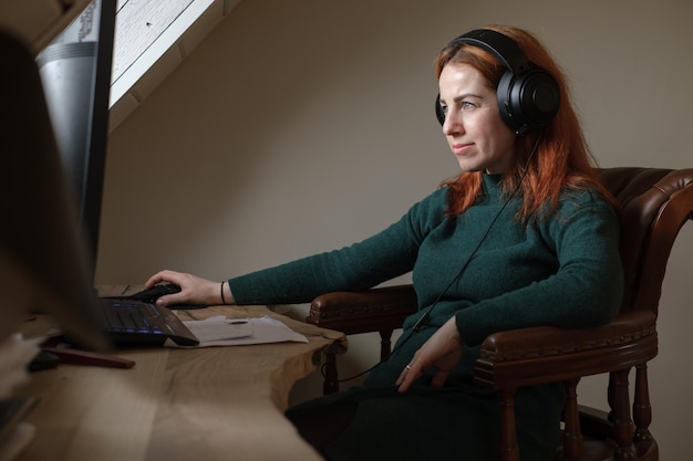 Woman listening to music in big headphones near computer