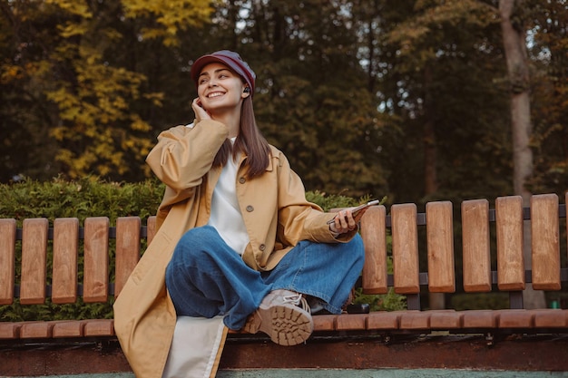 woman listening to music in earbuds while sitting with crossed legs on bench in park