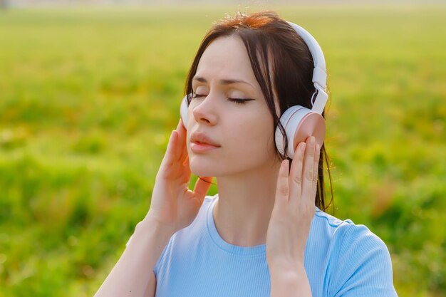 A woman in listening to music in headphones closing her eyes as Outside surrounded by naturedeep relaxation embracing the tranquility of the moment