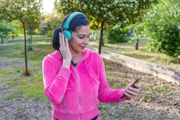 公園でヘッドフォンで音楽を聴いてスマートフォンを握っている女性