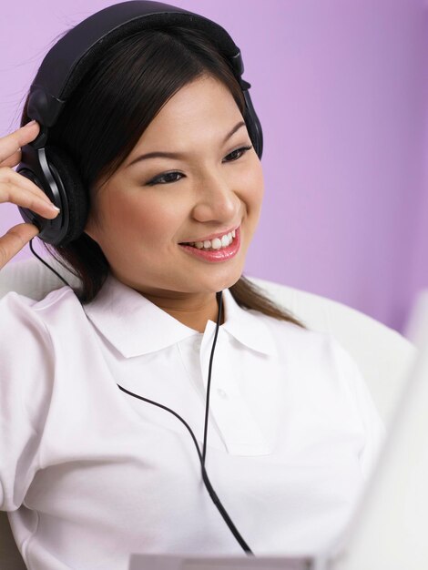 Woman listening music on headphones while using laptop at home