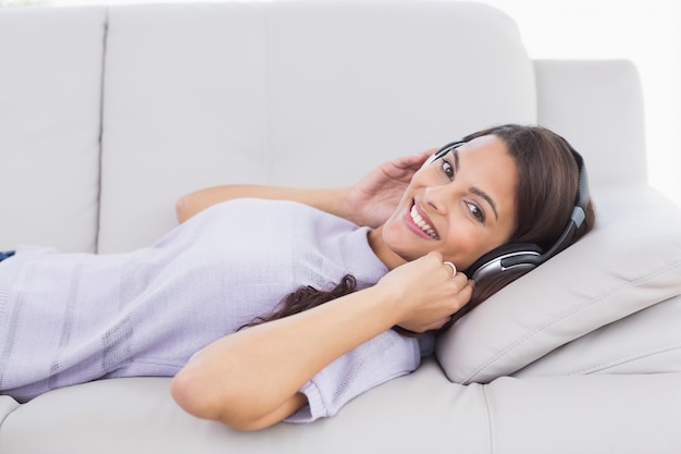 Woman listening music through headphones while lying on sofa