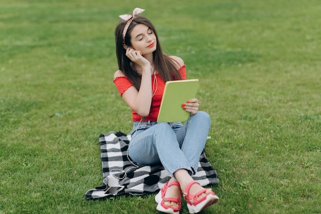 Woman listening music through headset and reading book in park