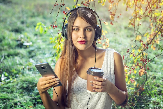 晴れた日にヘッドフォンを身に着けているあなたの電話で音楽を聴く女性。