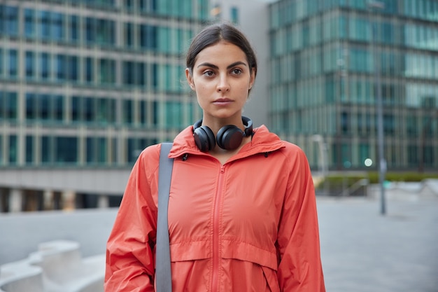 Woman listens radio online on workout break uses sound\
accessory keeps fitness goals strolls in urban city during daytime\
thinks about her future sport life wants to become fitness\
instructor