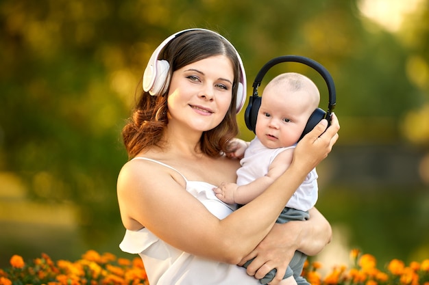 Woman and little boy in cordless headphones sit in public park