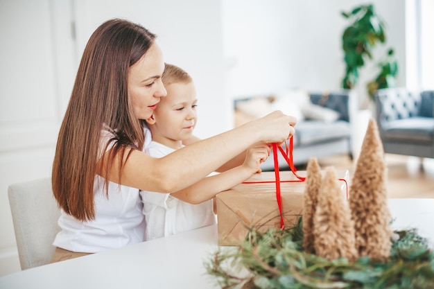 Женщина и маленький мальчик упаковывают коробку с рождественским подарком