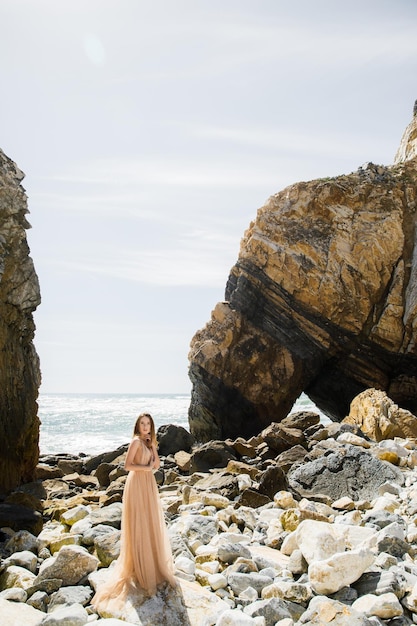 Woman in long dress near rocks and ocean