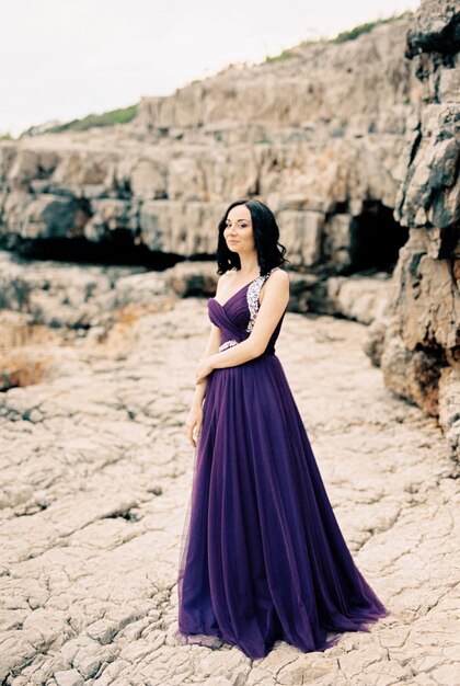 Woman in a long dress stands near the rocks