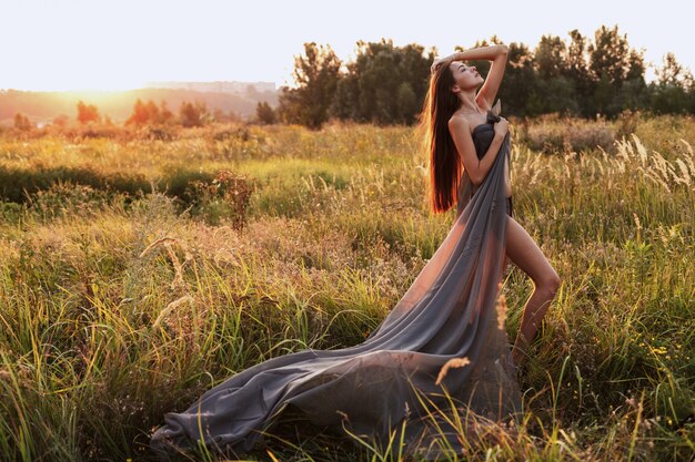 Woman in a long gray dress in a field at sunset