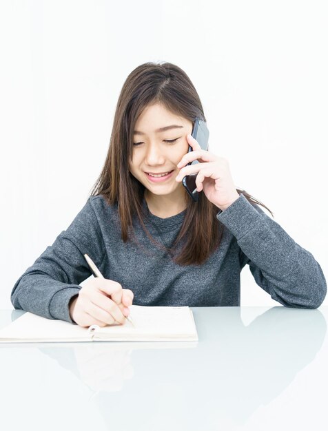 Foto donna con i capelli lunghi donna che usa il telefono cellulare e scrive un quaderno su sfondo bianco