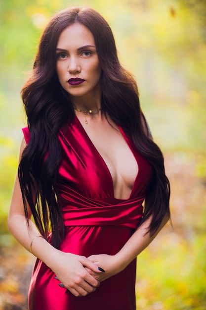 Donna in un vestito rosso lungo da solo nella foresta. favolosa e misteriosa immagine di una ragazza in una foresta oscura nel sole della sera. tramonto, la principessa si è persa.