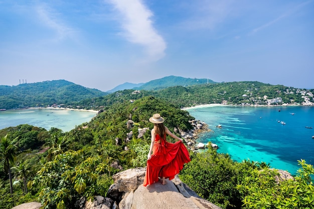 Nang Yuan Island의 인기 있는 관점에서 높은 바위에 서 있는 긴 빨간 드레스와 모자를 쓴 여성