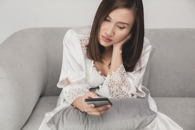 Woman in long sleepwear holding the smartphone in living room