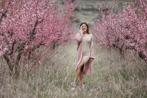 長いタイトなドレスを着た女性が、桃の木と桜の木の間に並ぶ道を歩く