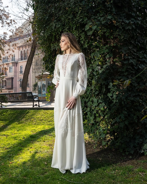 A woman in a long white dress stands in a park