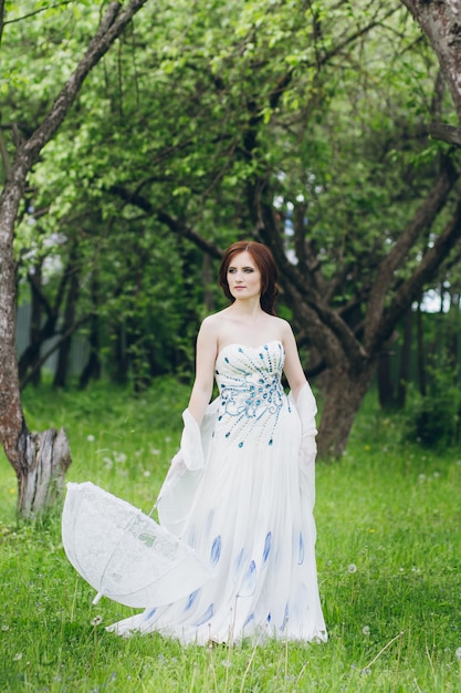 Женщина в длинном белом платье в летнем саду