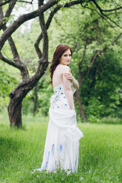 Woman in long white dress in summer garden