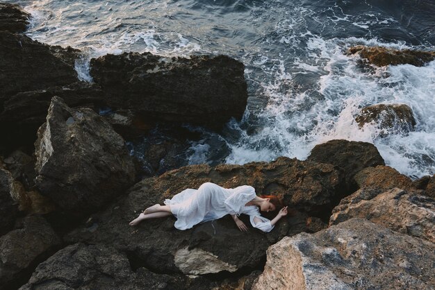 Woman in long white dress wet hair lying on a rocky cliff\
nature landscape