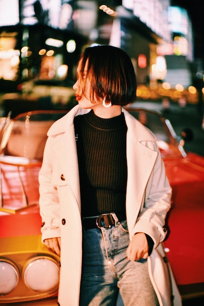 woman looking away while leaning on car in city at night