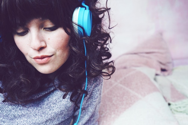 家でヘッドフォンで音楽を聴いている女性